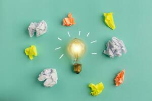 Great idea concept with crumpled colorful paper and a light bulb on a wooden table. photo