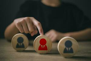 Hand touching a human icon on wood. Choice of employee leader from the crowd. Human resource management, HR, recruitment, leadership, and team building. photo