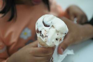 niño mano participación vainilla hielo crema en un gofre cono. foto