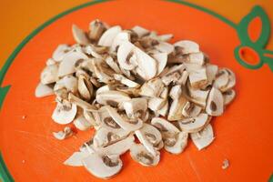 Sliced champignon mushrooms on a chopping board on orange background photo