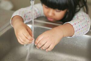 child washing hands with water at kitchen sink photo