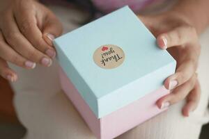 women hand putting a thank you sticker on a gift box photo