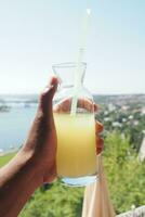 holding a glass of orange juice against blue sky photo