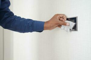 hand with cloth wiping a light switch at the wall photo