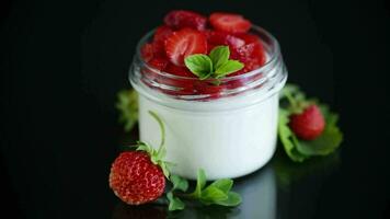 Sweet homemade yogurt with fresh ripe strawberries in a glass jar isolated on black background video