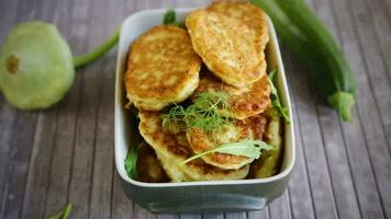 fried vegetable pancakes from squash and zucchini with herbs, on a light wooden table. video