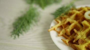 fried potato cheese vegetable waffles with bacon and onions in a plate, on a wooden table. video