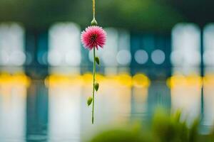 a pink flower hanging from a string in front of a lake. AI-Generated photo