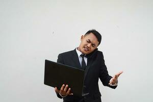 Portrait Young Asian businessman multitasking, calling with mobile phone while working with laptop isolated on white background photo