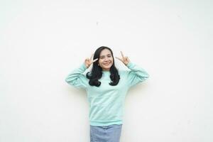 Portrait Indonesian beautiful woman wearing light blue sweater with peace hand sign, smile face isolated on white background photo