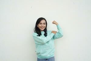 Portrait Indonesian beautiful woman wearing light blue sweater with strong, healthy gesture, show muscles, lifting his arm isolated on white background photo