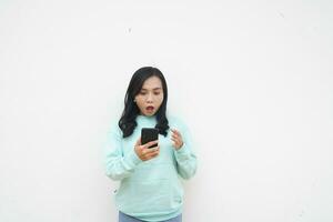 Portrait Indonesian beautiful woman wearing light blue sweater with surprised gesture look at mobile phone isolated on white background photo