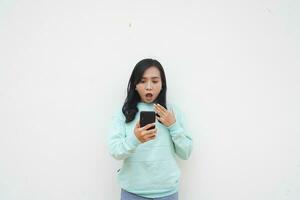 Portrait Indonesian beautiful woman wearing light blue sweater with surprised gesture look at mobile phone isolated on white background photo