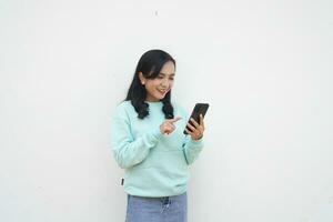 retrato indonesio hermosa mujer vistiendo ligero azul suéter con contento y sonrisa cara Mira a móvil teléfono aislado en blanco antecedentes foto