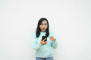 Portrait Indonesian beautiful woman wearing light blue sweater with surprised gesture look at mobile phone isolated on white background photo