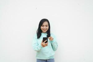 Portrait Indonesian beautiful woman wearing light blue sweater with happy and smile face look at mobile phone isolated on white background photo