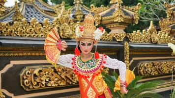 niña vistiendo balinés tradicional vestir con un bailando gesto en balinés templo antecedentes con Mano admirador, corona, joyas, y oro ornamento accesorios. balinés bailarín mujer retrato foto