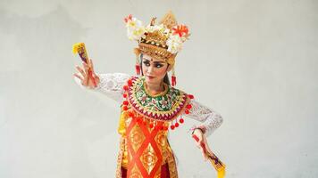 girl wearing Balinese traditional dress with a dancing gesture on white background with hand-held fan, crown, jewelry, and gold ornament accessories. Isolated Balinese dancer woman portrait photo