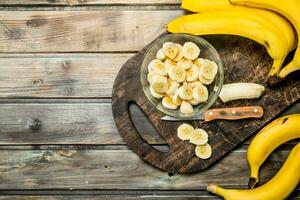 Bananas and banana slices in a plate on a black chopping Board with a knife. photo