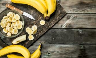 Bananas and banana slices in a plate on a black chopping Board with a knife. photo