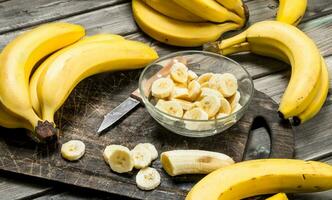 Bananas and banana slices in a plate on a black chopping Board with a knife. photo