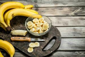 Bananas and banana slices in a plate on a black chopping Board with a knife. photo