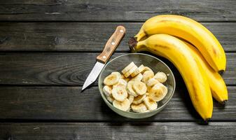 Fragrant bananas and banana slices in a glass bowl with a knife. photo