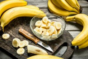 Bananas and banana slices in a plate on a black chopping Board with a knife. photo