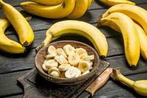 Bananas and banana pieces in a wooden plate on a cutting Board with a knife. photo