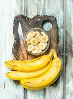 Bananas and banana slices in a glass bowl on an old cutting Board. photo