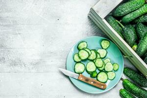 Cucumbers on a tray and slices of cucumber on a plate with a knife. photo