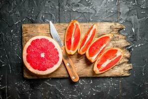 Pieces of grapefruit on a cutting Board with a knife. photo