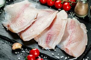 crudo pescado filete con especias y Tomates en un Roca tablero. foto