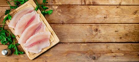 Raw fish fillet with parsley on a cutting board. photo