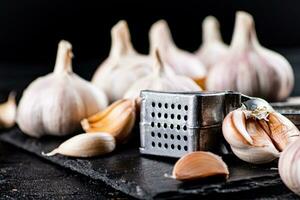 Garlic with a garlic press on a stone board. photo