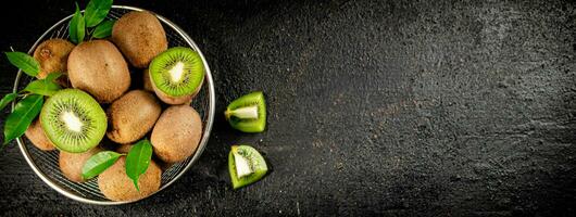 Ripe kiwi with leaves in a colander on the table. photo