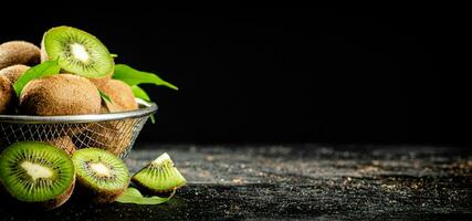 Ripe kiwi with leaves in a colander on the table. photo