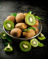 Ripe kiwi with leaves in a colander on the table. photo