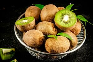 Ripe kiwi with leaves in a colander on the table. photo