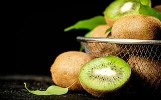 Ripe kiwi with leaves in a colander on the table. photo