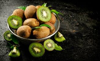 Ripe kiwi with leaves in a colander on the table. photo