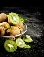 Ripe kiwi with leaves in a colander on the table. photo