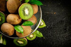 Ripe kiwi with leaves in a colander on the table. photo