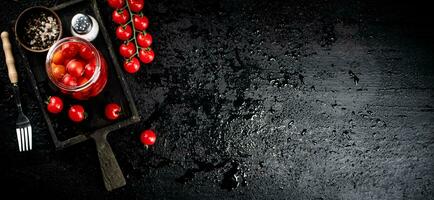 Pickled tomatoes in a glass jar on a cutting board. photo