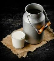 Rustic milk in a can and a glass on the table. photo