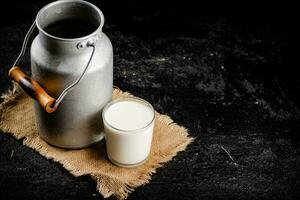 rústico Leche en un lata y un vaso en el mesa. foto