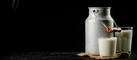 Rustic milk in a can and a glass on the table. photo