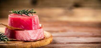 A steak of raw tuna on a cutting board with a sprig of rosemary. photo