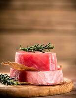 A steak of raw tuna on a cutting board with a sprig of rosemary. photo