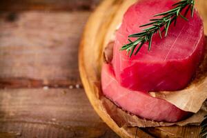 A steak of raw tuna on a cutting board with a sprig of rosemary. photo